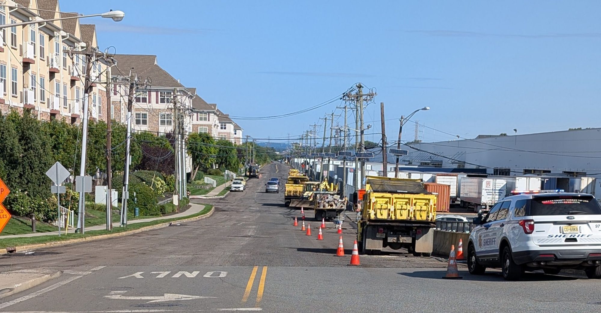 Photo looking down County Rd Ext showing a milled road with construction vehicles and many cones closing a lane.