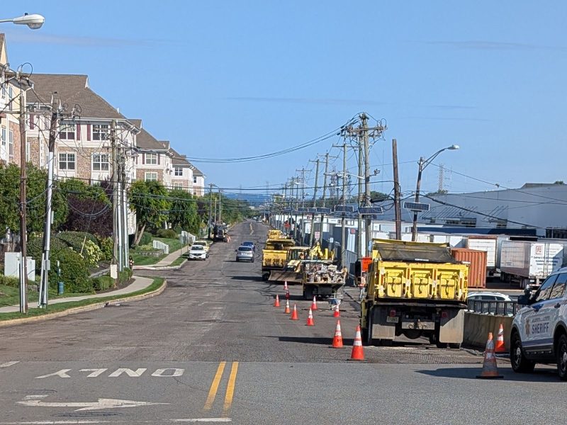 Photo looking down County Rd Ext showing a milled road with construction vehicles and many cones closing a lane.